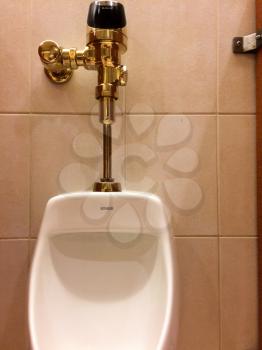 Urinal in mens public restroom bathroom with luxury gold plumbing valve handle