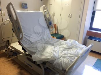 Hospital room bed empty raised up with used bedsheets