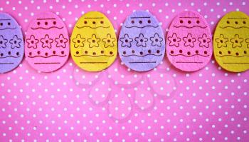 Row of decorated felt easter eggs lilac, pink and yellow on a pink polka dots background
