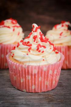 White cupcakes with vanilla icing and red candies in a pink polka dots paper.