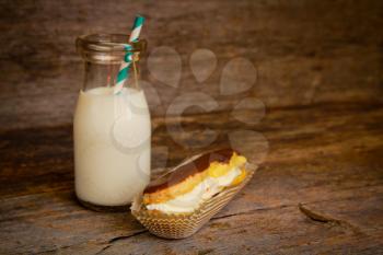 Chocolate eclair in a paper and an old fashion bottle of milk on a wooden surface