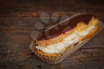 Chocolate eclair in a paper on a wooden surface