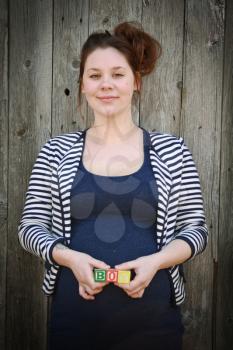 Portrait of a pregnant young and smiling woman holding the word boy made with wooden blocks on her belly