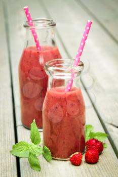 Strawberry smoothie freshly made in a jar with a pink straw on rustic wood
