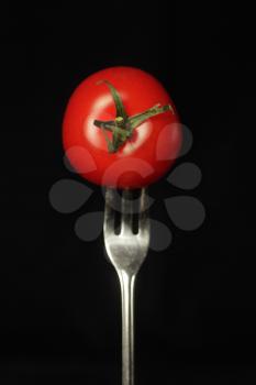 Red tomato facing us on a fork on a black background
