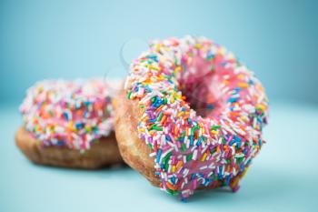 Two donuts with pink icing and candies on a blue pastel background