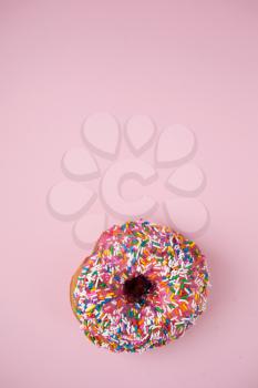 Donut with pink icing and candies on a pink pastel background
