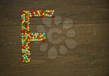 Letter F from alphabet made with star shape candy on a wooden background