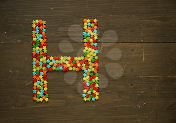 Letter H from alphabet made with star shape candy on a wooden background