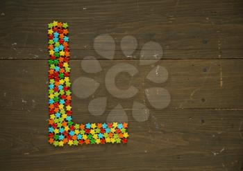 Letter L from alphabet made with star shape candy on a wooden background