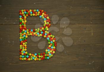 Letter B from alphabet made with star shape candy on a wooden background
