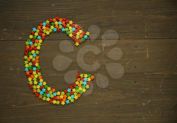 Letter C from alphabet made with star shape candy on a wooden background