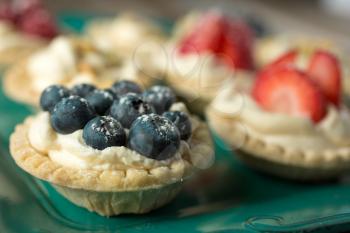 Blueberry, strawberry and pistachios tartlets and spoons on a wooden table