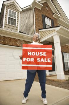 Royalty Free Photo of a Portrait of middle-aged African-American female outside house with for sale sign.