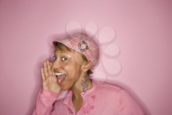 Portrait of smiling young African-American adult woman on pink background yelling and smiling at unseen person.
