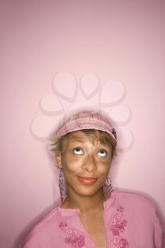 Head and shoulder portrait of young African-American adult woman on pink background looking up with eyes.