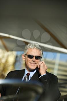 Royalty Free Photo of a Businessman in a Suit Sitting at a Patio Table Outside Talking on a Cellphone and Smiling