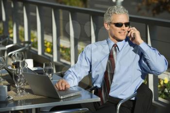 Royalty Free Photo of a Businessman in a Suit Sitting at a Patio Table With a Laptop and Talking on a Cellphone