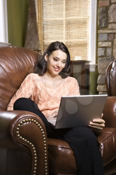Royalty Free Photo of a Young Woman Sitting in a Leather Chair Looking at a Laptop Computer