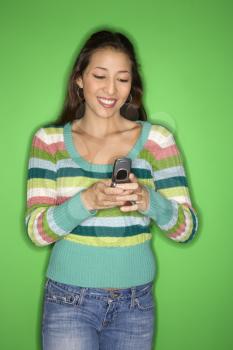Portrait of smiling Multi-racial teen girl dialing cellphone standing in front of green background.