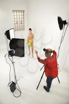 Young African American male adult photographer and young female Caucasian adult model in studio.