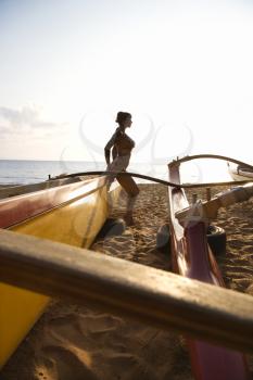 Silhouette of sexy Caucasian woman in bikini beside outrigger canoe on beach in Maui, Hawaii, USA.