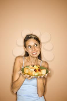 Portrait of young adult woman holding a plate of fruit.