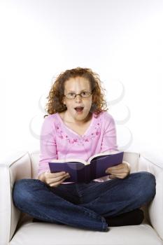 Royalty Free Photo of a Little Girl Sitting and Reading Book Looking Surprised