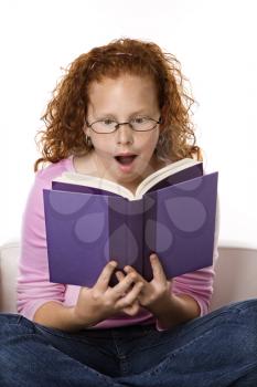 Royalty Free Photo of a Little Girl Sitting and Reading Book Looking Surprised