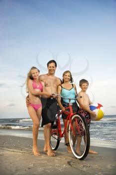 Caucasian family of four walking on beach.