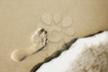 Royalty Free Photo of a Footprint in Sand Next to a Wave of Water