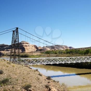 Royalty Free Photo of a Suspension Bridge Over River With Rock Cliffs in Utah.