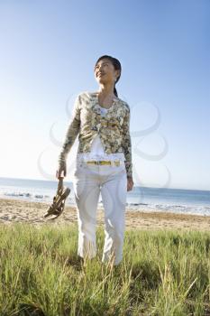 Royalty Free Photo of a Young Female Walking Down the Beach Carrying Her Sandals