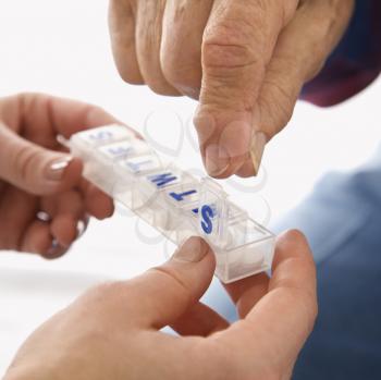 Mid-adult Caucasian female hands holding medication case for  an elderly Caucasian male.