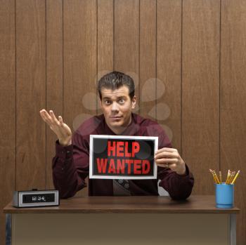 Royalty Free Photo of a Businessman Sitting at a Desk Holding a Help Wanted Sign