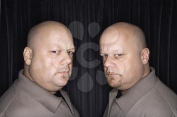 Caucasian bald mid adult identical twin men looking sternly at viewer.