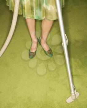 Royalty Free Photo of a Close-Up of a Woman's Feet With a Vacuum Against a Green Retro Carpet