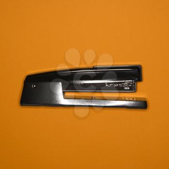 Royalty Free Photo of a Black Stapler on an Orange Background