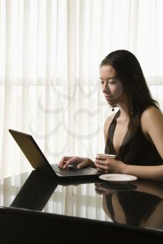 Royalty Free Photo of a Woman Typing on a Laptop and Drinking Coffee