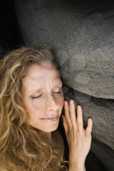 Caucasian mid-adult woman smiling with eyes closed leaning against rock.