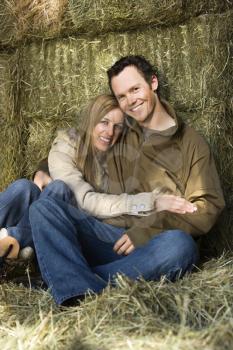 Royalty Free Photo of a Couple Sitting on Hay Hugging and Smiling