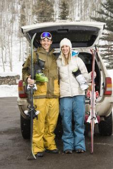 Royalty Free Photo of a Couple Wearing Winter Clothes Standing by an Automobile With Ski Equipment Smiling