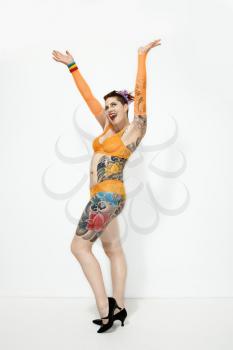 Adult caucasian woman with tattoos standing with arms out.