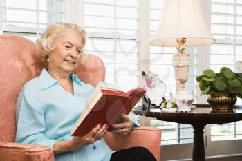 Royalty Free Photo of an Older Woman Sitting in a Chair Reading a Book