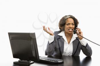 Businesswoman sitting at office desk with computer talking on telephone looking upset.