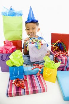 Royalty Free Photo of a Boy Sitting Smiling Wearing a Party Hat With Wrapped Presents