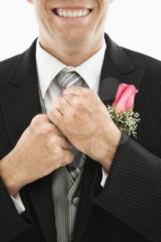 Close up of Caucasian groom adjusting his tie.