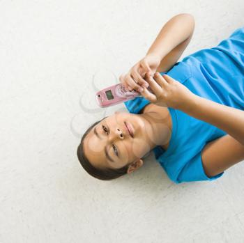 Asian preteen girl lying on back on floor text messaging on cell phone.