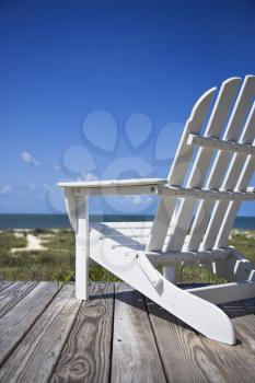 Royalty Free Photo of an Empty White Adirondack Chair Facing the Beach