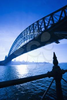 Low angle view of Sydney Harbour Bridge at dusk with harbour and distant Sydney skyline, Australia.